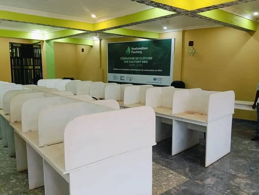 Salle de formation aménagée en postes individuels, avec l'affiche de clôture du programme The Factory DRC.
